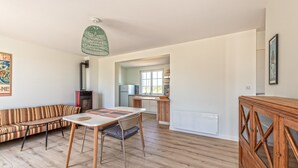 Amplia sala de estar con sofá, mesa de comedor y piso de madera. Se ve una cocina al fondo.