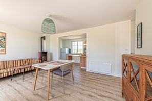 Un vaste espace de vie comprenant un canapé, une table à manger et un plancher en bois. On aperçoit une cuisine au fond.
