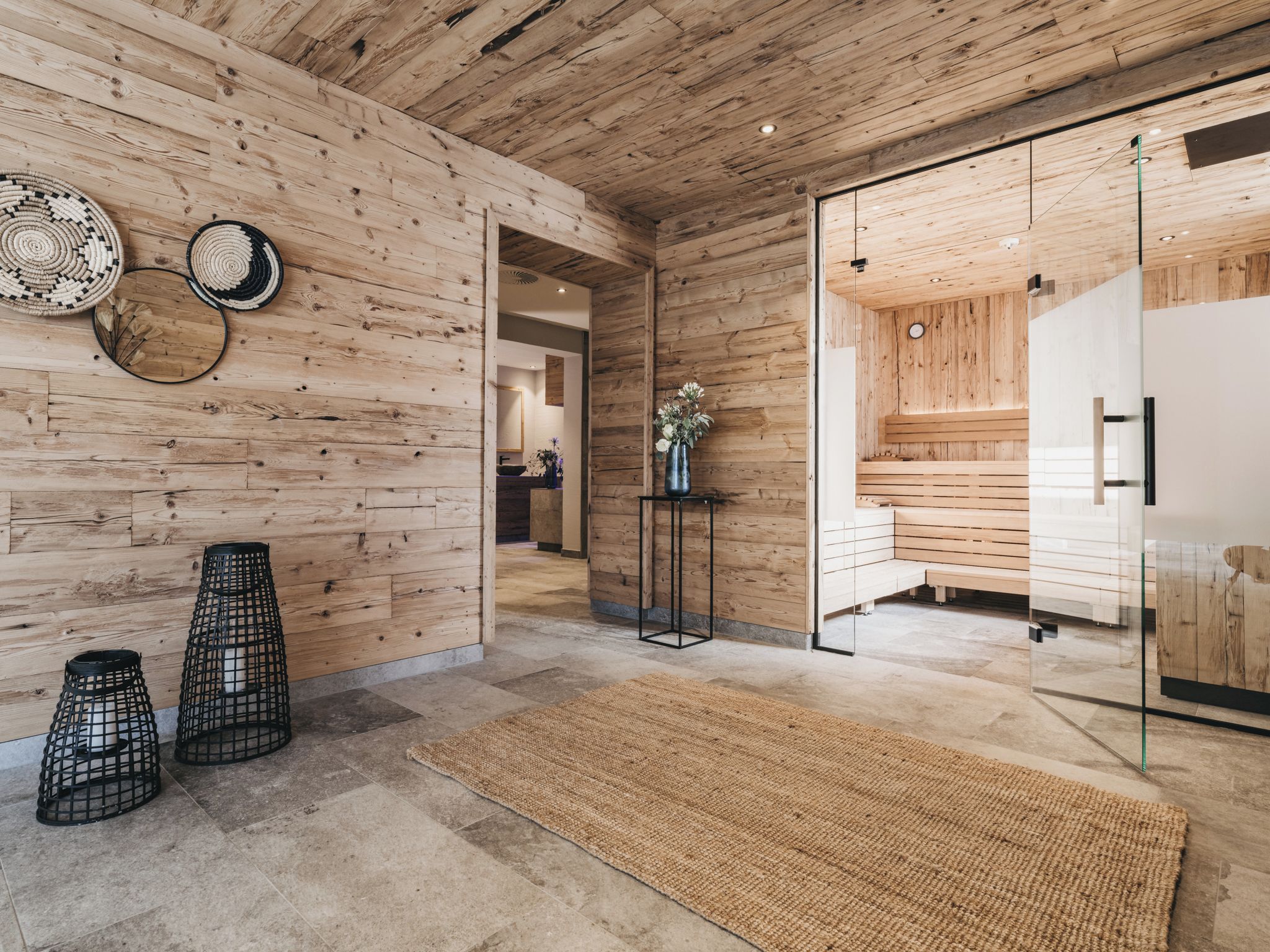 A modern interior with wooden walls, a glass door leading to a sauna area, and a woven rug on the floor.