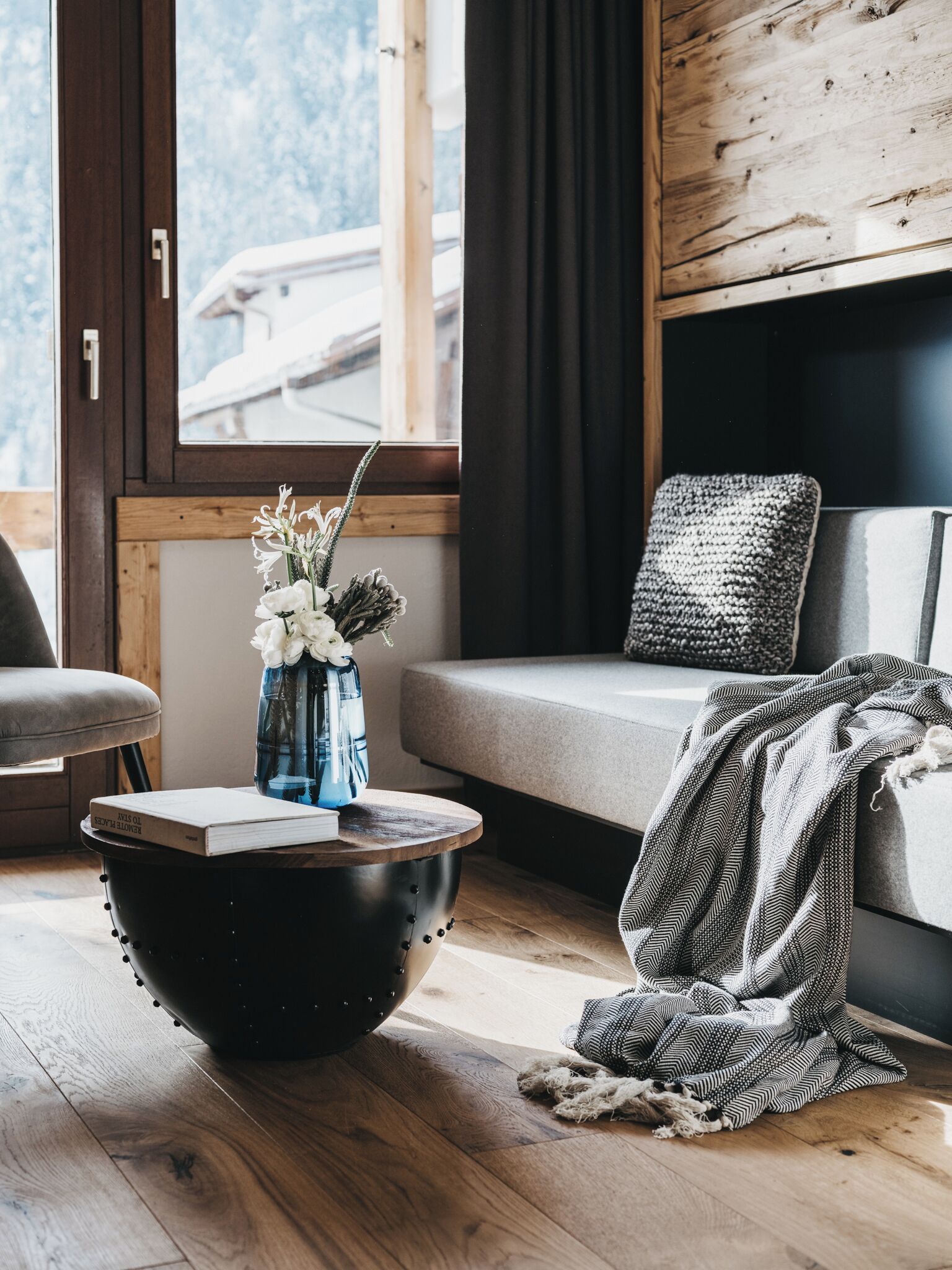 Un salon moderne avec un plancher en bois, une table basse noire, un canapé et une fenêtre donnant sur un immeuble.