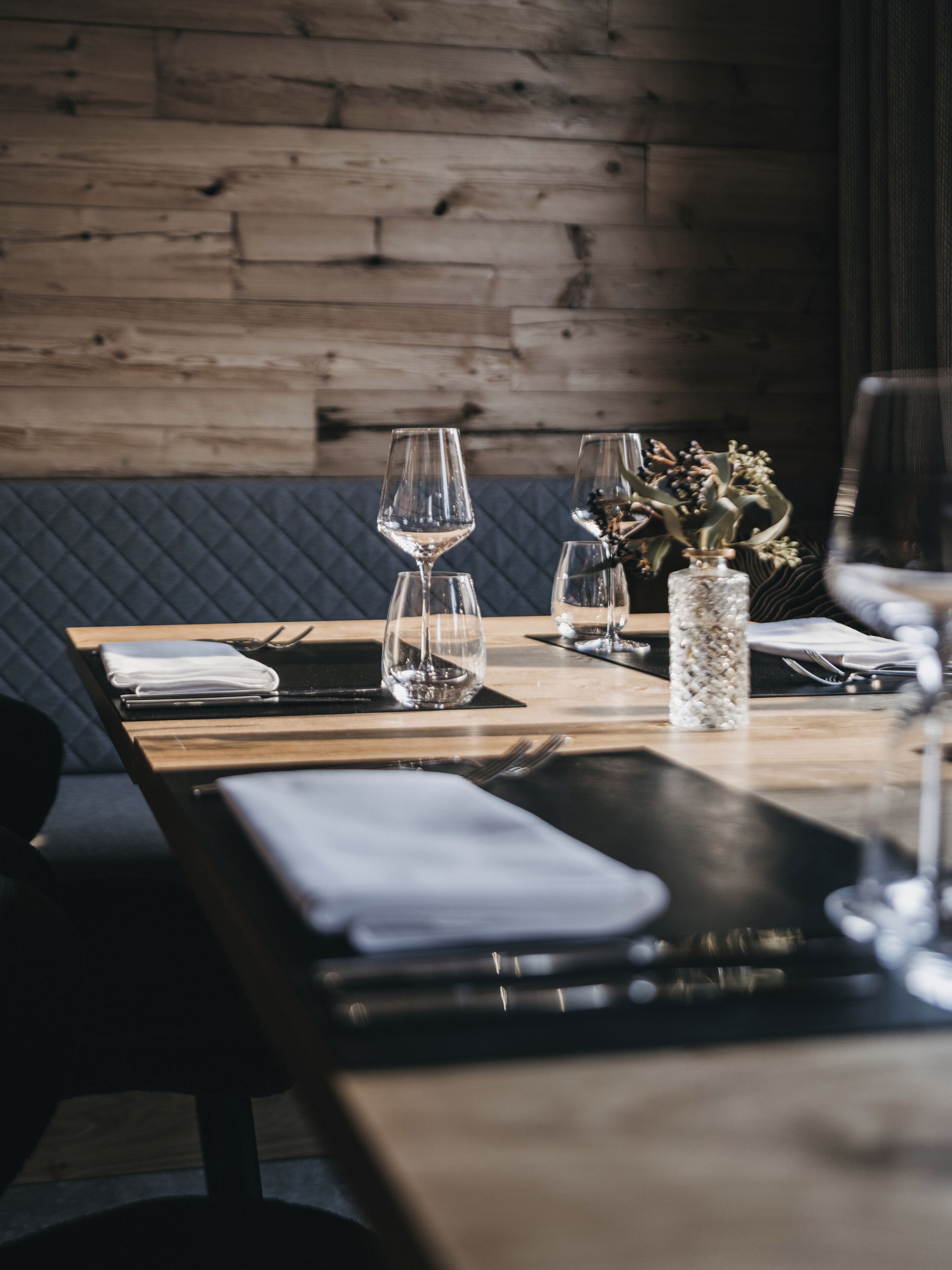 A dining table set with wine glasses, a vase with dried flowers, and a folded napkin.