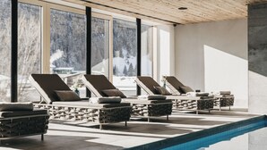 Una piscina interior moderna con sillones de descanso y grandes ventanales que ofrecen vista a un paisaje nevado.