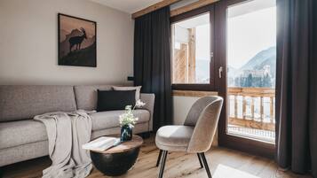 Ein modernes Wohnzimmer mit einer Couch, einem Sessel, einem Couchtisch und einem großen Fenster mit Blick auf einen Berg und ein Gebäude.