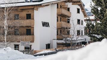 A modern multi-story building with the name "VAYA" prominently displayed. It features wooden balconies and a snow-covered landscape.