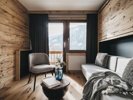 Una habitación acogedora con paredes de madera, un sofá, una silla y una mesa con un libro y un jarrón.