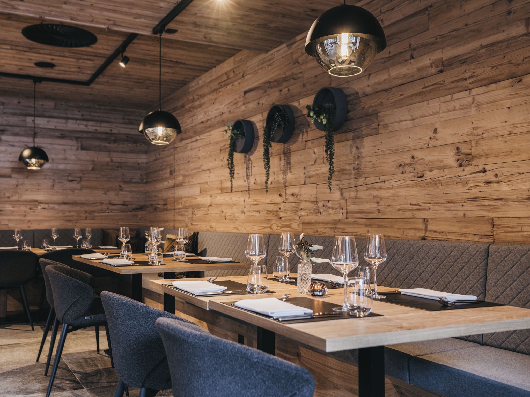 L’intérieur d’un restaurant présente des murs en bois, des suspensions lumineuses et des tables soigneusement disposées, accompagnées de chaises.