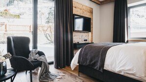 Habitación de hotel moderna con una cama grande, un televisor montado en una pared de madera y vistas a un paisaje nevado a través de amplias ventanas.