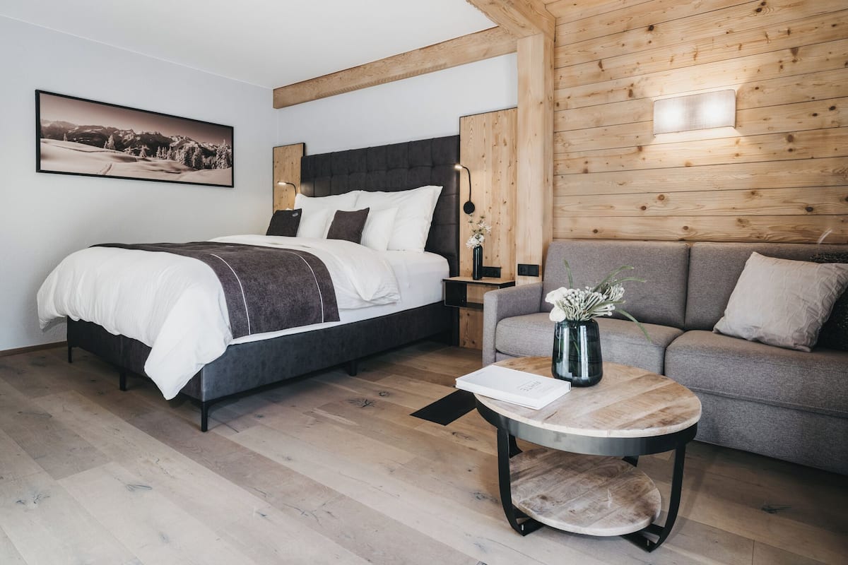 Un dormitorio moderno con cama, sofá, una mesita redonda y una lámpara de pared.