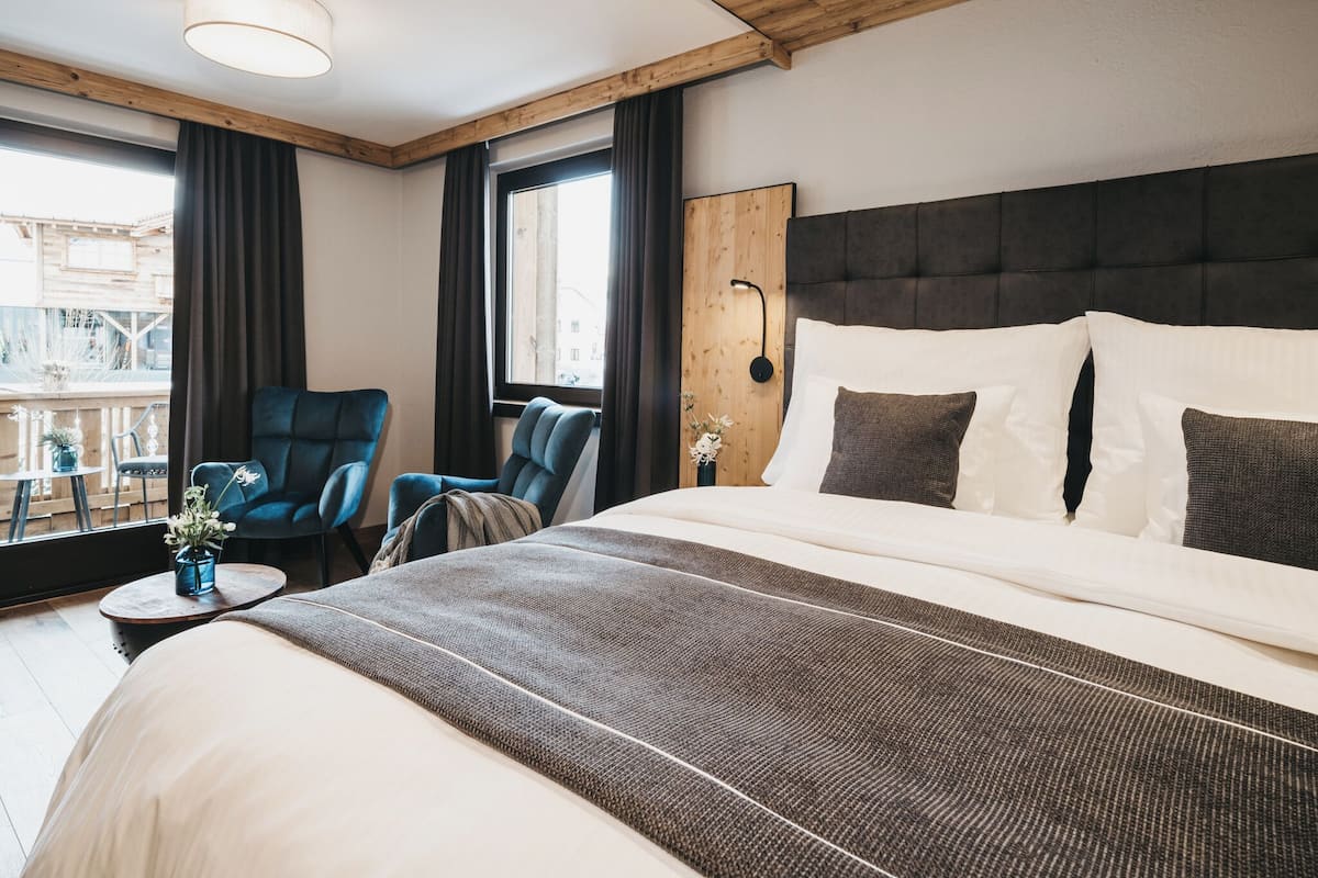 Una habitación de hotel moderna con una cama grande, techo de madera, vistas a la ciudad y un área de descanso con sillas.