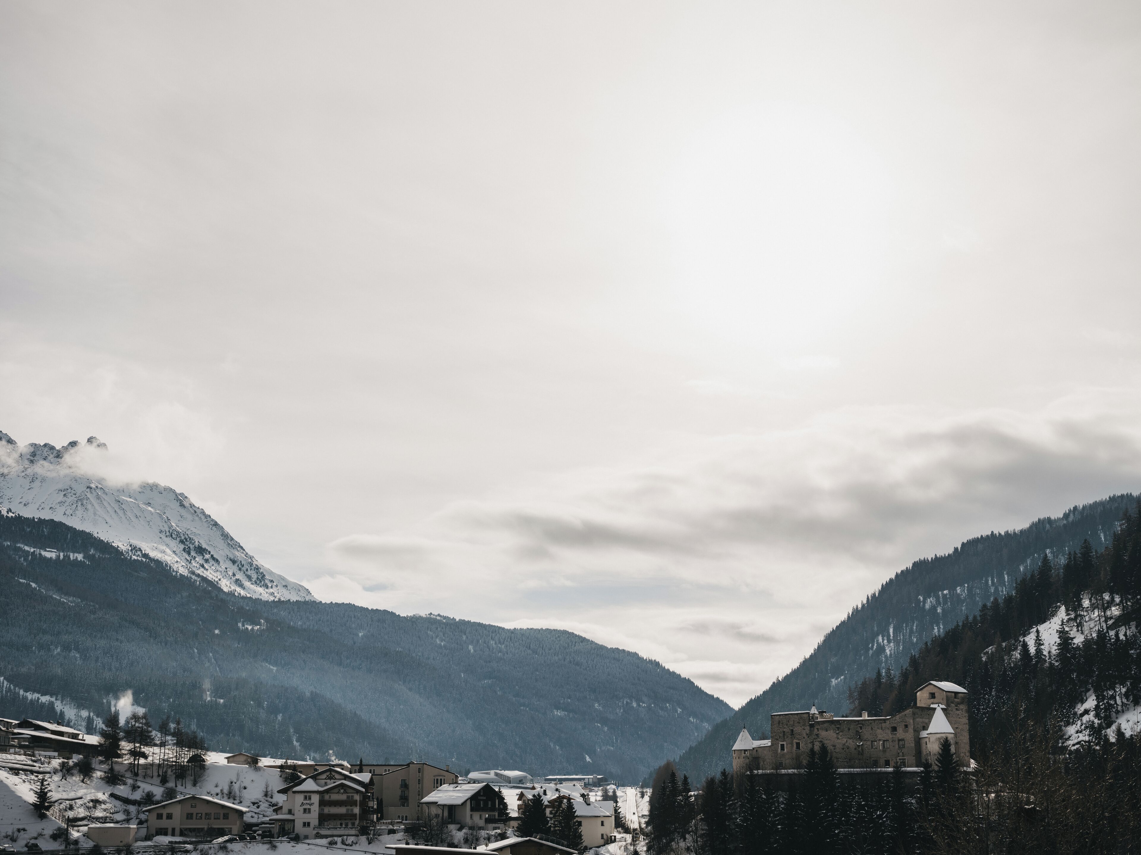 Un village de montagne aux bâtiments traditionnels, avec une structure qui ressemble à un château et des sommets enneigés.