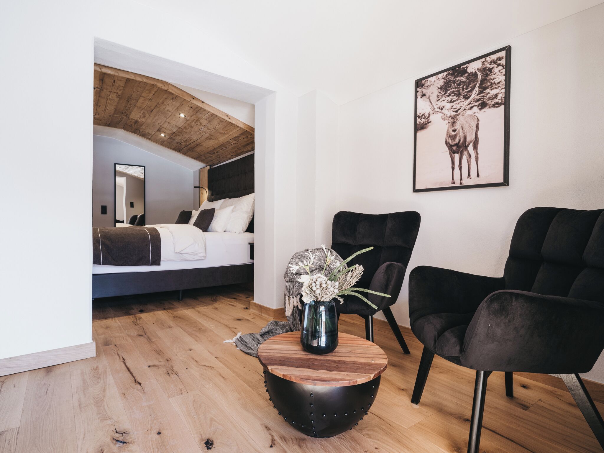 Une chambre à coucher moderne avec un plafond de style industriel, un lit, une table basse avec un vase et deux chaises noires.