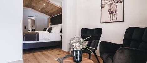 Une chambre à coucher moderne avec un plafond de style industriel, un lit, une table basse avec un vase et deux chaises noires.