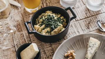 Ein Holztisch mit verschiedenen Speisen, darunter eine Schüssel Kartoffelpüree, ein Teller mit Käse und Trauben, ein Glas Orangensaft und eine Schüssel Obstsalat.