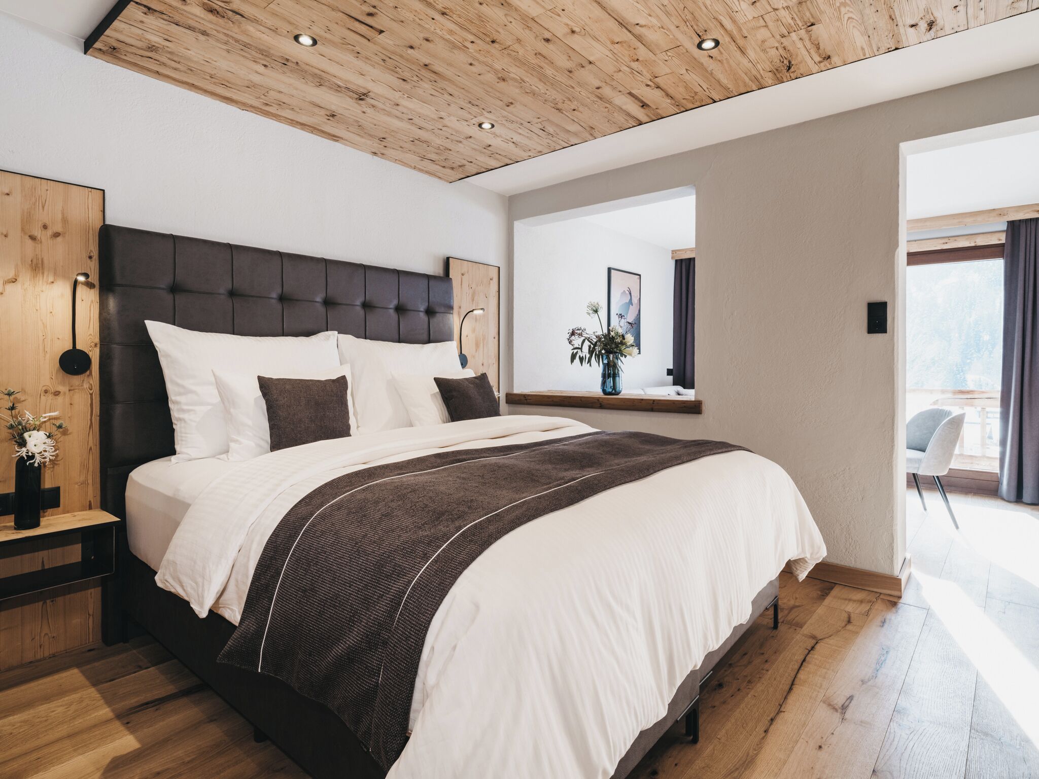 Een moderne slaapkamer met een groot bed, houten plafond en uitzicht op het omliggende landschap.