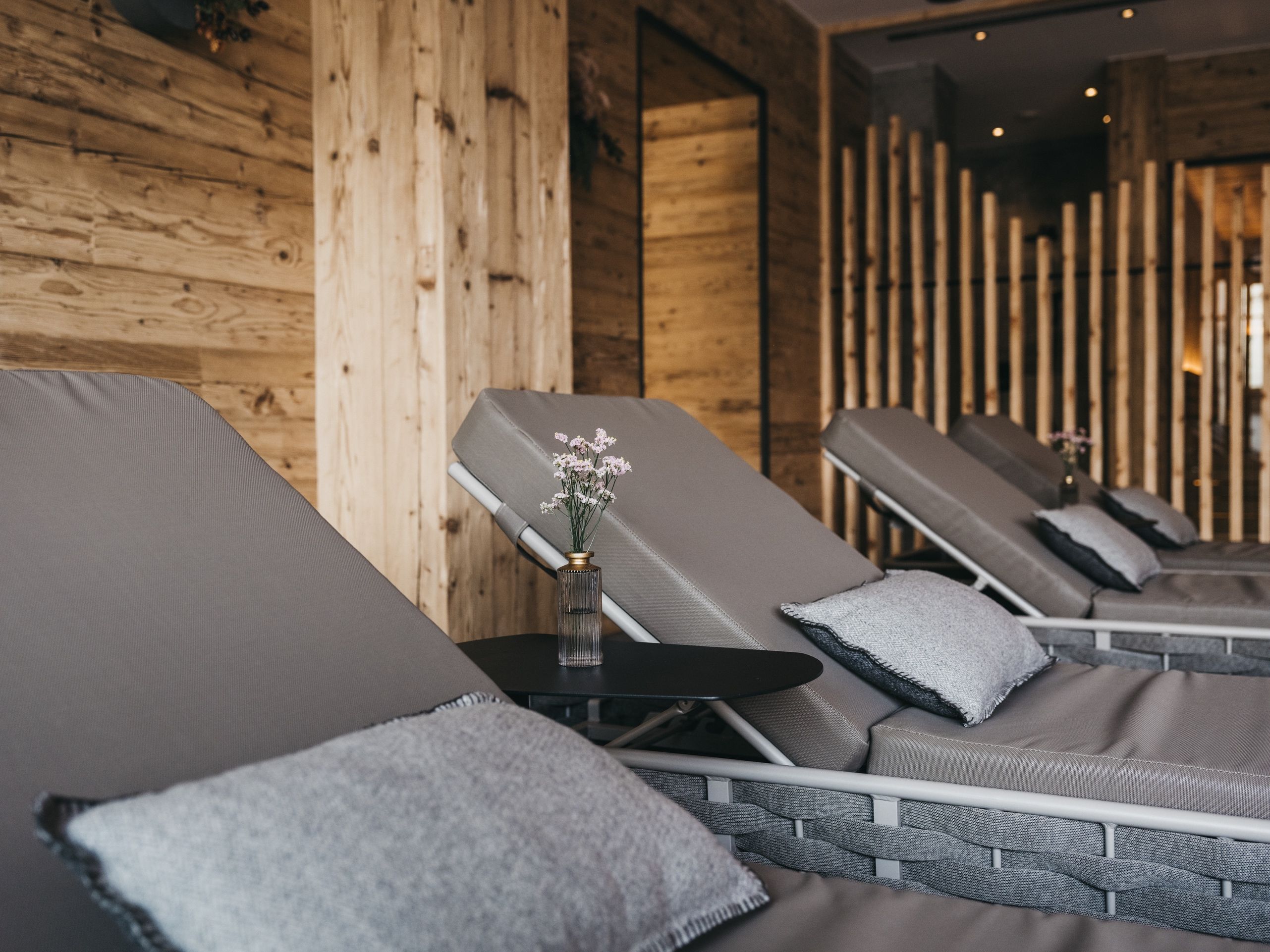 A room with wooden walls, a small table with a vase, and reclining chairs with cushions.
