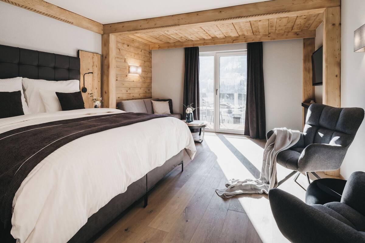 Un hotel moderno con una cama grande, una zona de estar con una silla y vistas a la ciudad desde la ventana.