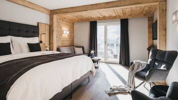 Ein modernes Hotelzimmer mit einem großen Bett, einer Sitzecke mit einem Sessel und Blick auf die Stadt durch das Fenster.