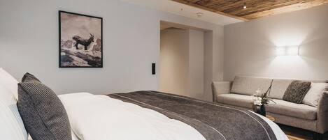 A bedroom with a wooden ceiling, a bed with white and dark bedding, a gray sofa, and a framed picture on the wall.