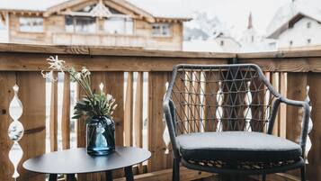 A wooden deck with a wicker chair and a small table, a vase with flowers, and a building in the background.
