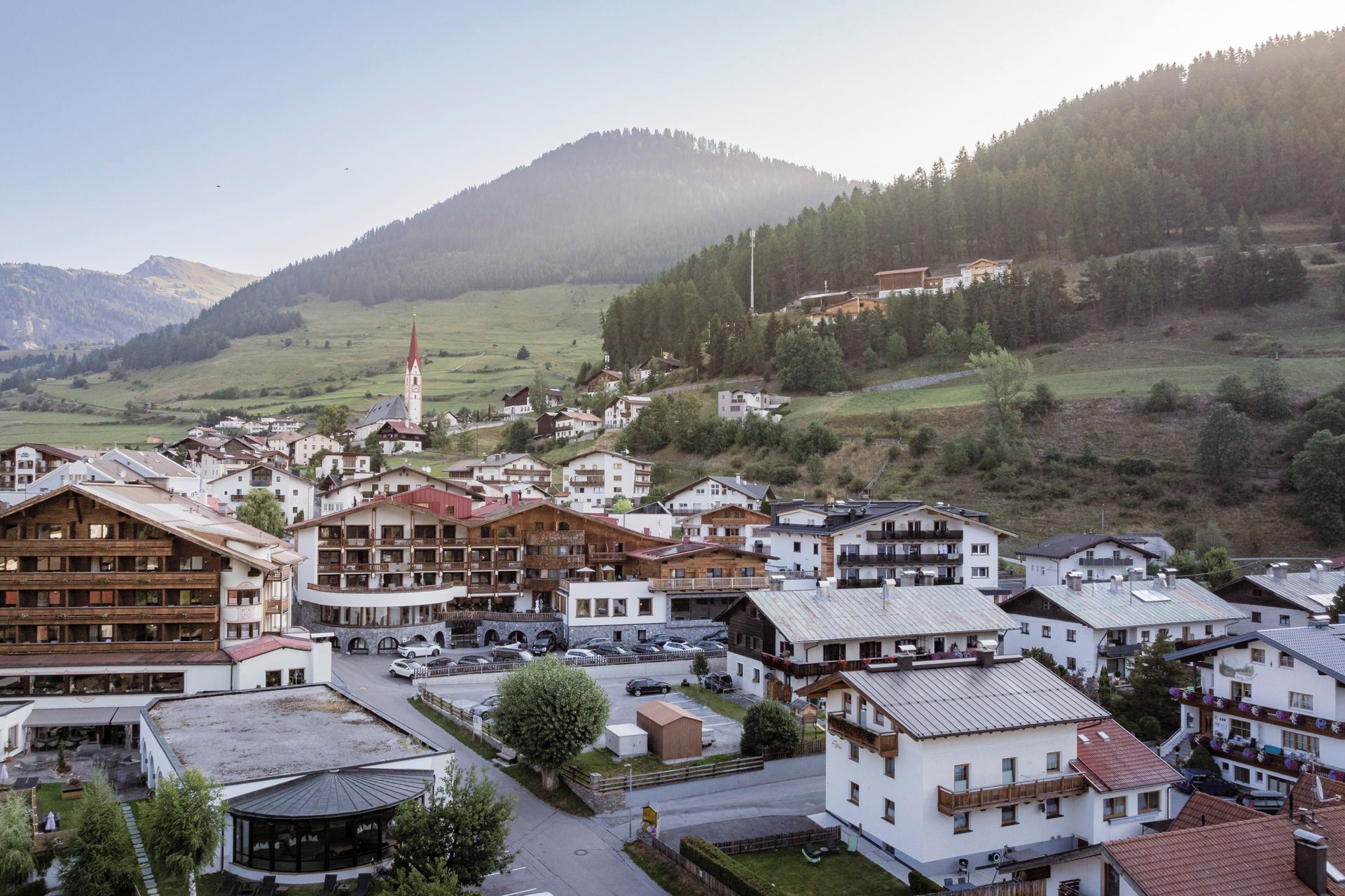 Un pueblo de montaña con una iglesia destacada, diversas edificaciones residenciales y un estacionamiento.