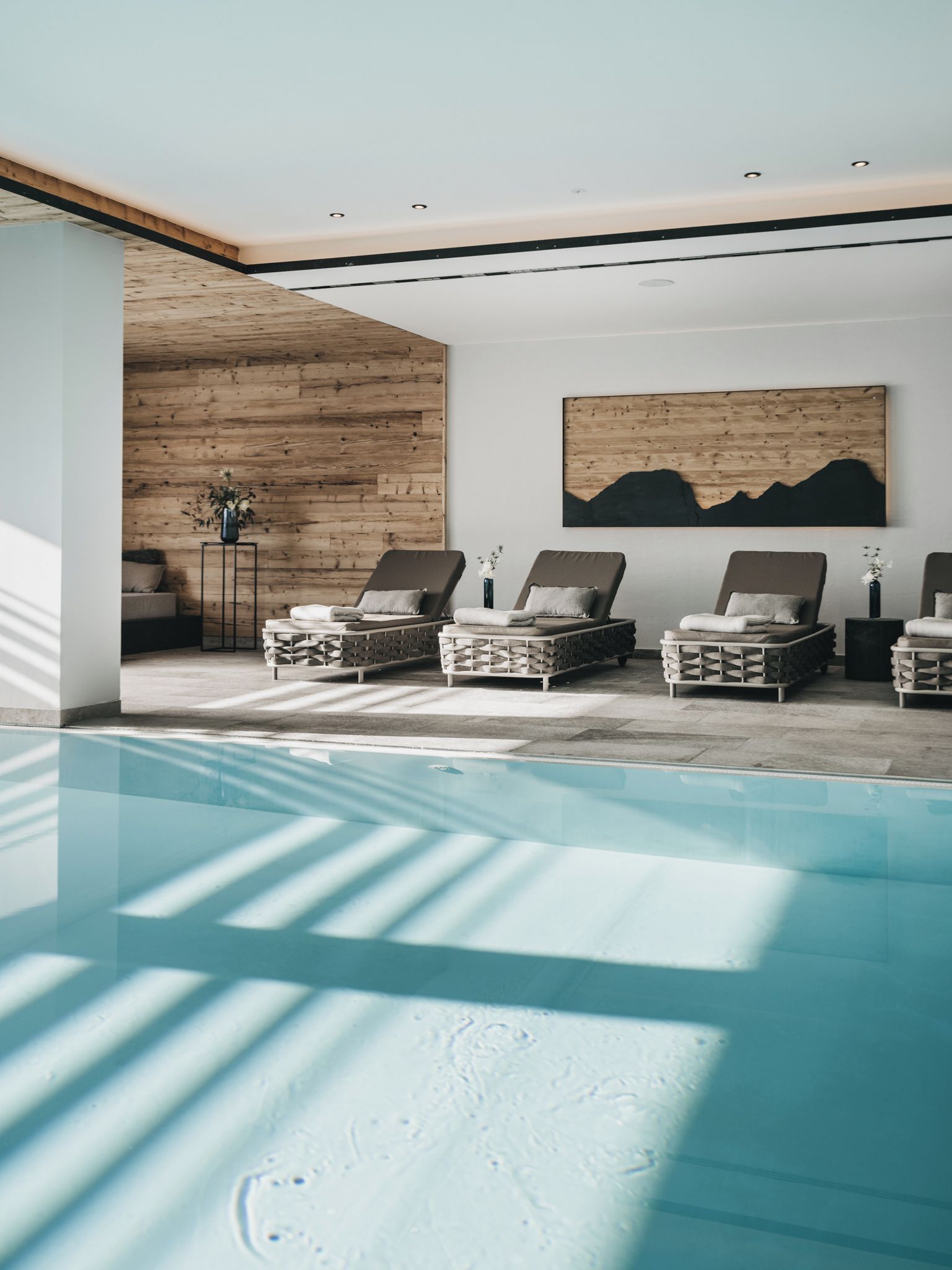 Ein moderner Poolbereich im Innenbereich mit Liegestühlen und einer Holzwand.