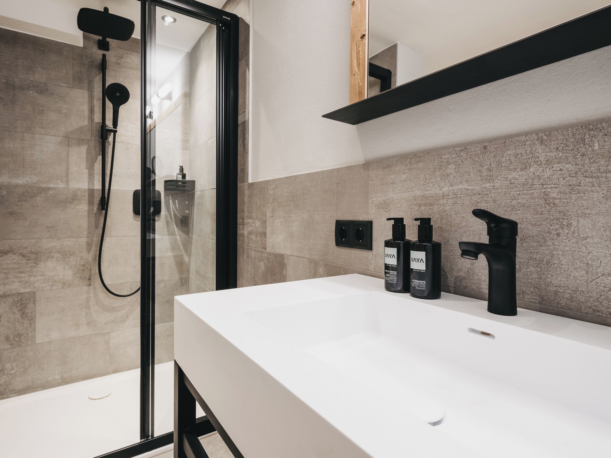 A modern bathroom with a glass shower enclosure, a white sink, and black toiletries.