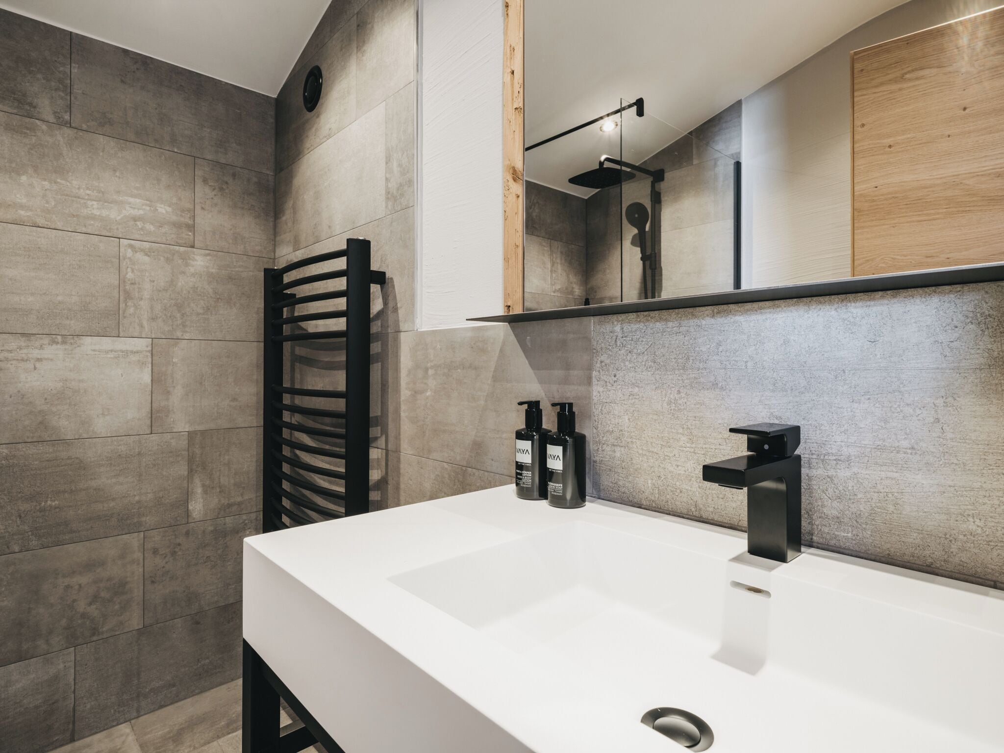 Un baño moderno con lavamanos blanco, grifo negro y un perchero para toallas.