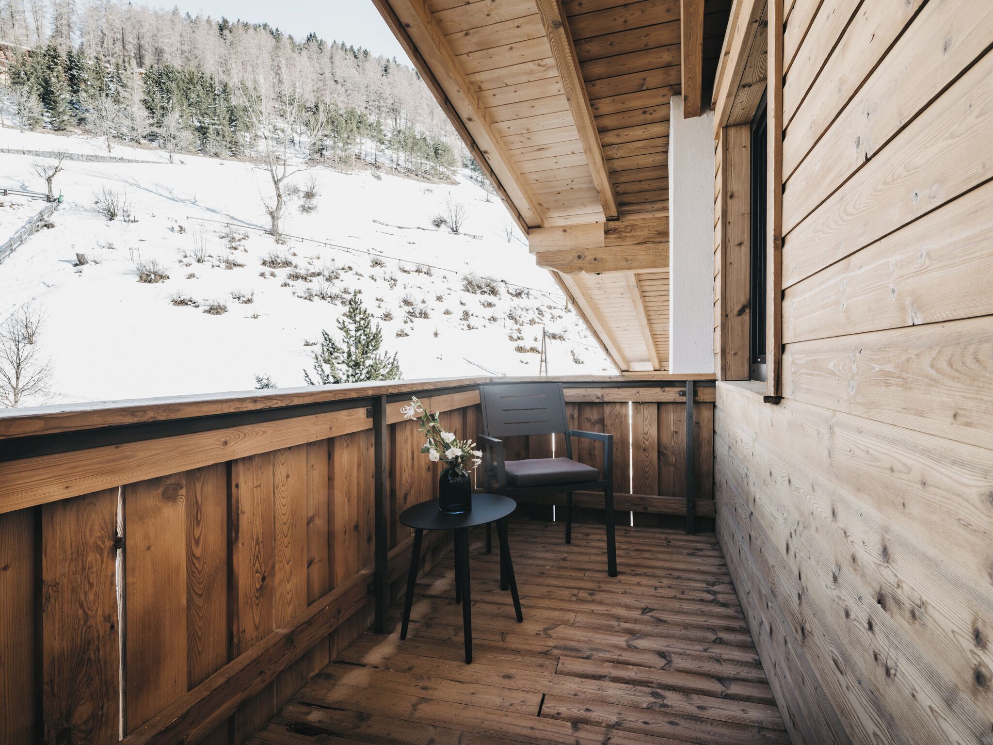 Ein Holzbalkon mit Blick auf eine verschneite Landschaft und einem Stuhl.