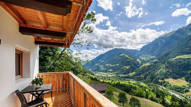 A wooden balcony with a table and chairs, overlooking a valley with mountains and a river. - Apartment 'Bergchalet Prantach W75' with Mountain View, Shared Terrace and Wi-Fi (San Martino In Passiria)