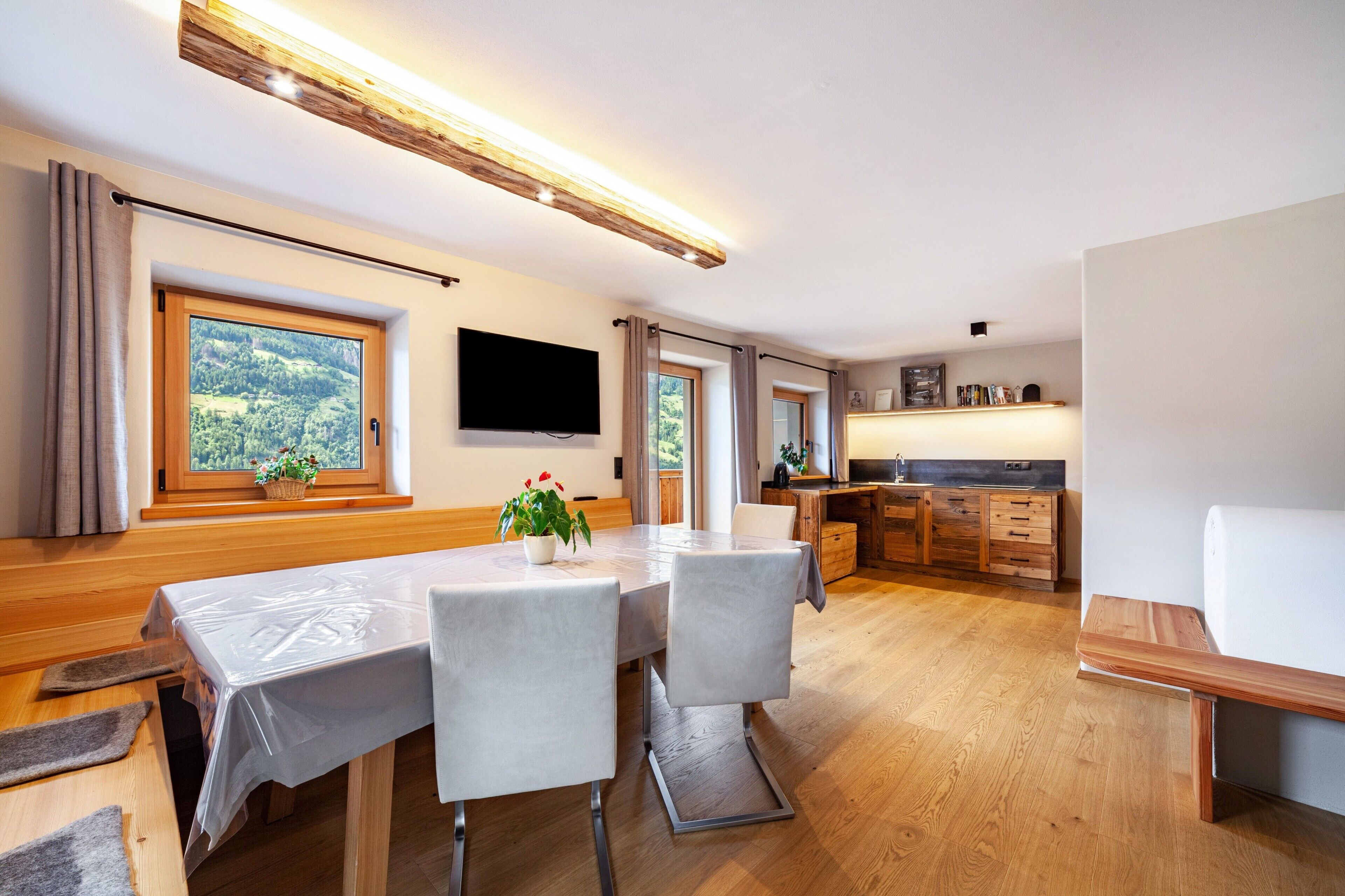 Eine moderne Küche mit Holzschränken, ein Essbereich mit Tisch und Stühlen sowie ein großes Fenster mit Blick ins Grüne.
