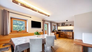 A modern kitchen with wooden cabinets, a dining area with a table and chairs, and a large window with a view of greenery. - Apartment 'Bergchalet Prantach W75' with Mountain View, Shared Terrace and Wi-Fi (San Martino In Passiria)