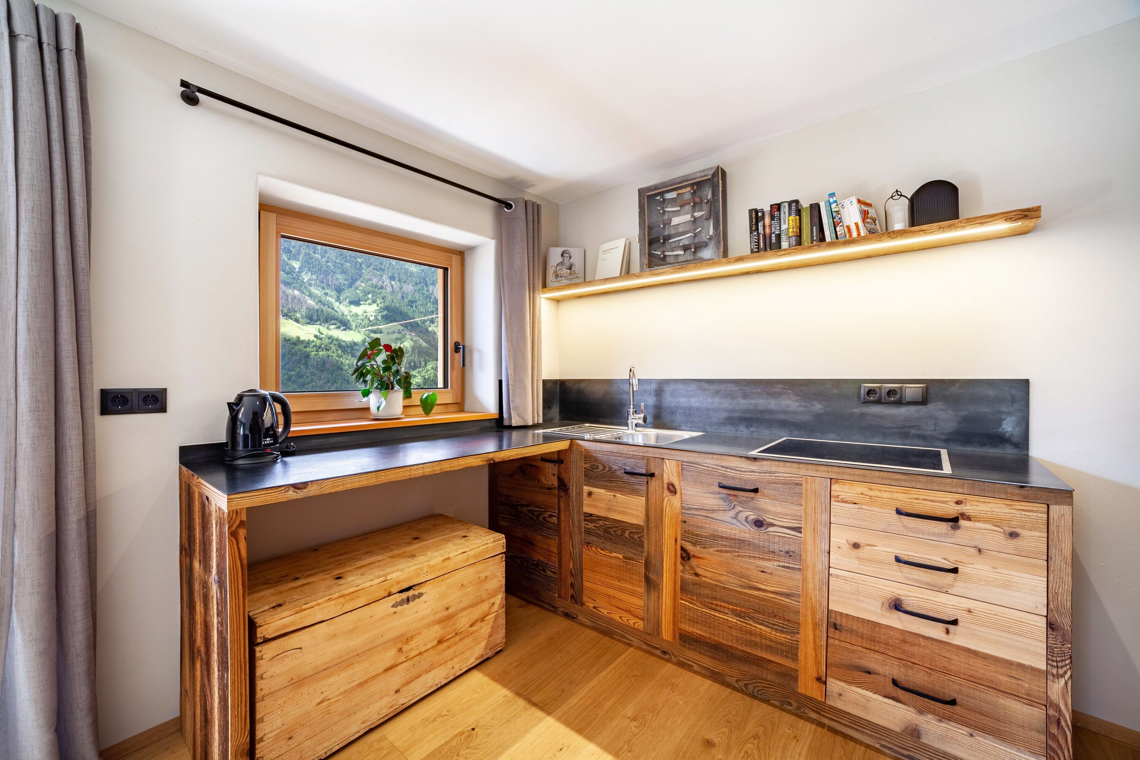 Eine kleine Küche mit einer Holz Arbeitsplatte, eingebauten Schränken, einem Fenster mit Blick auf Grünflächen und einem Regal mit Büchern und Dekoration.