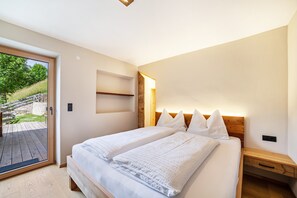 A bedroom with a bed, bedside tables, a wooden headboard, a sliding glass door, and a view of greenery outside.