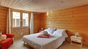 A wooden cabin bedroom with a bed, a nightstand, a chair, and a window.