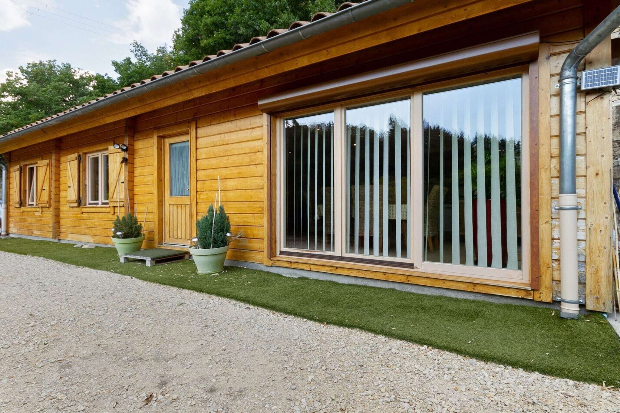 Eine Holzhütte mit großen Schiebeglastüren, einer kleinen Veranda mit Stufen und Topfpflanzen.