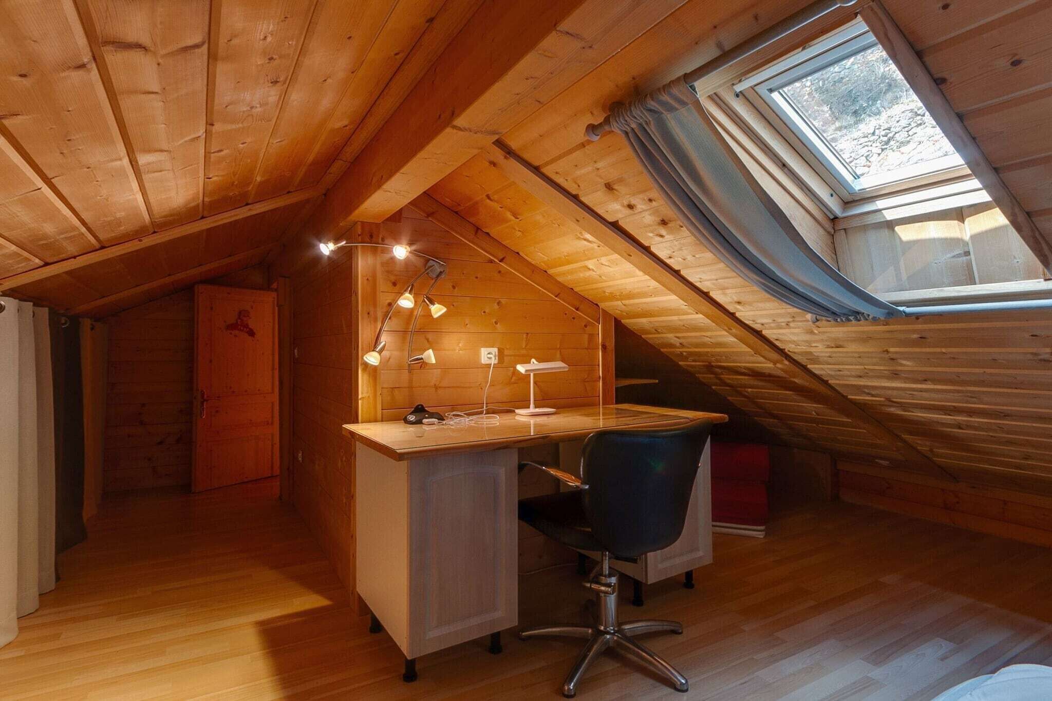 A small attic room with a wooden desk, a chair, and a skylight.