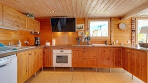 A modern kitchen with wooden cabinets, a built-in oven, a large window with a view, and a flat-screen TV mounted above the counter.