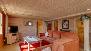 A cozy log cabin interior with a wooden ceiling, a television, a sofa, and a coffee table.