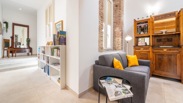 Ein Wohnzimmer mit grauem Sofa, Holzschrank, Bücherregal und einem Spiegel.