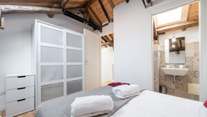 Ein Schlafzimmer mit Bett, Schrank, Badezimmer mit Waschbecken und Spiegel sowie einem Oberlicht.
