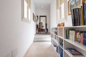 Un couloir avec un escalier menant à un piano, des étagères à livres et des tableaux encadrés accrochés aux murs.