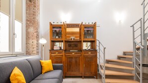 Eine Treppe mit Metallgeländer, ein graues Sofa mit gelben Kissen und ein Holzschrank mit Glastüren.