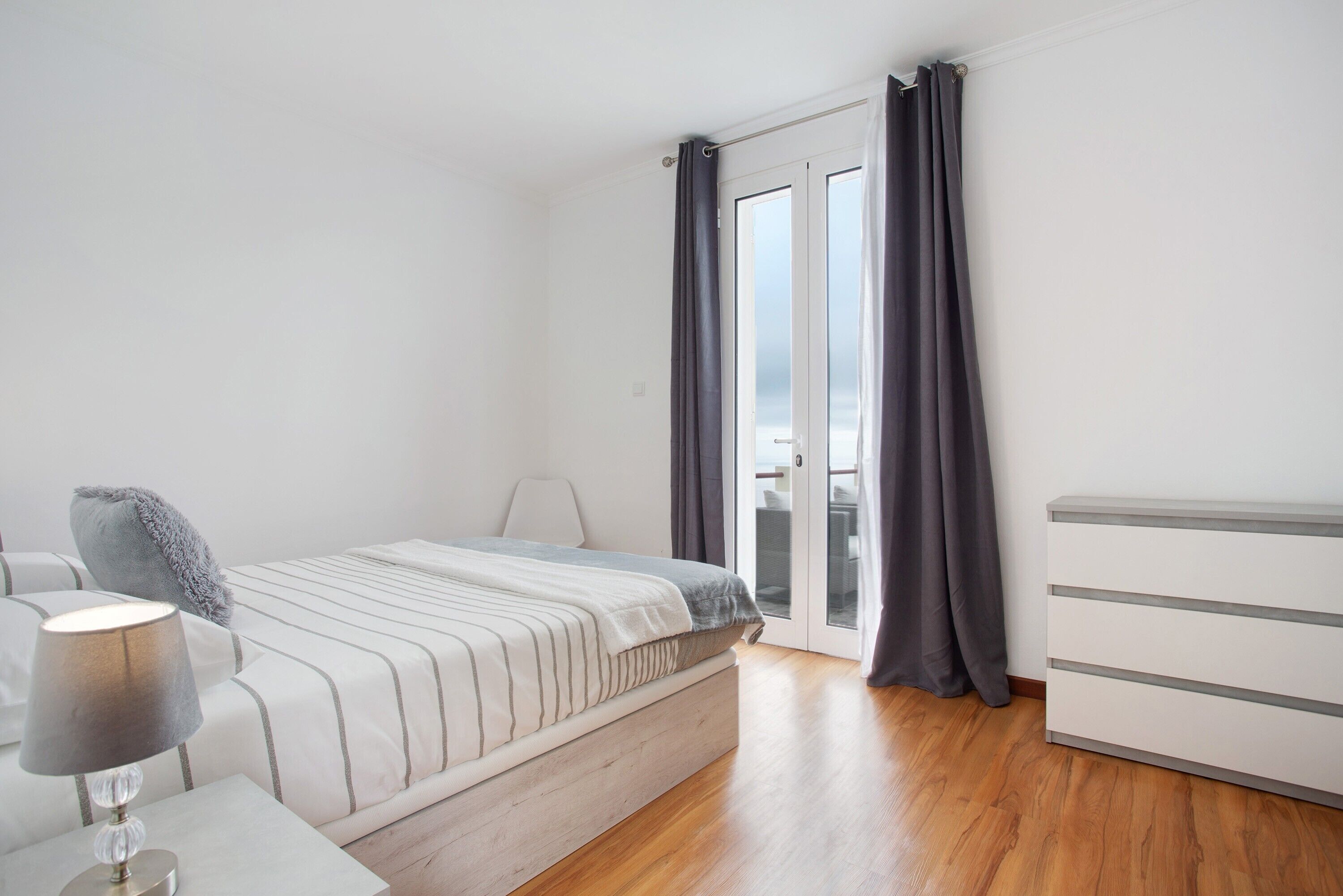 Une chambre à coucher avec un lit, une table de chevet, une lampe et une vue à travers une porte vitrée.