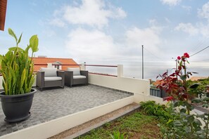 Une terrasse sur le toit, agrémentée d’un pot de fleurs, de deux fauteuils en osier et offrant une vue sur le paysage urbain.