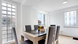 A dining area with a wooden table, four chairs, a bottle, and a fruit bowl. - Holiday Home 'Simão House' with Private Terrace, Private Garden and Wi-Fi (Calheta)