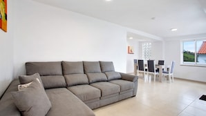 A modern living room with a sectional sofa, a dining table with chairs, and a large window. - Holiday Home 'Simão House' with Private Terrace, Private Garden and Wi-Fi (Calheta)