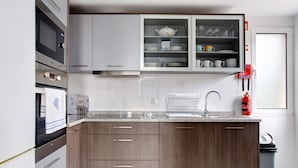A modern kitchen with a built-in microwave, oven, and stainless steel sink. - Holiday Home 'Simão House' with Private Terrace, Private Garden and Wi-Fi (Calheta)