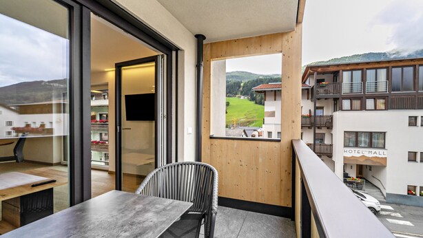 A balcony with a table and chair, a wooden wall, and a view of a hotel and mountains.