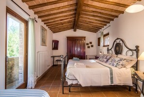 Un dormitorio con techo de madera, una cama con colcha estampada, un radiador y una ventana con cortinas.
