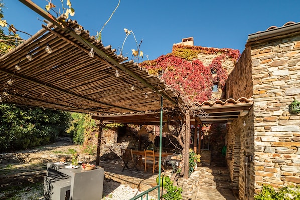 An outdoor patio with a pergola, stone walls, and a stone building with ivy.